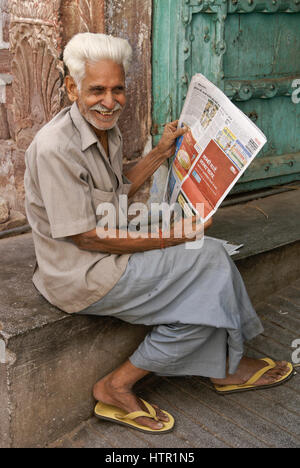 Uomo anziano giornale di lettura al di fuori della sua casa, Jodhpur, Rajasthan, India Foto Stock