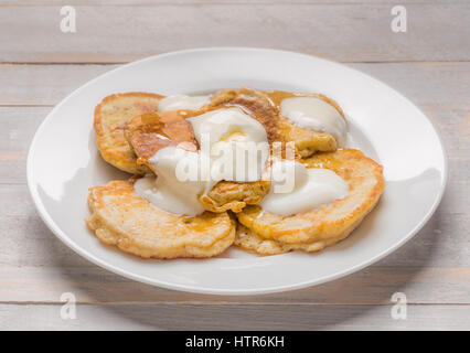 Individuale piccole frittelle di scotch servita su una piastra bianca con yogurt e miele Foto Stock