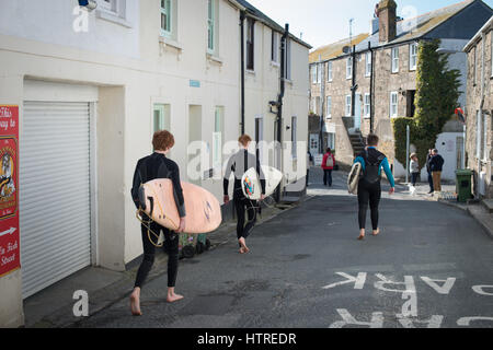 Ragazzi adolescenti indossando muta portare surf boarders passato cottages in St Ives, Cornwall, Inghilterra. Foto Stock