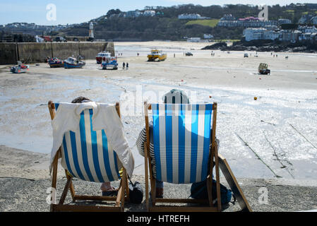 Due persone seduti su sedie a sdraio sul porto parete durante una giornata di sole a St Ives, Cornwall, Inghilterra. Foto Stock