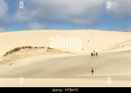 Giovani salire Te Paki dune di sabbia come cloud getta ombra sulla parte del pendio, enormi dune bianche di un preferito attrazione turistica e un luogo divertente nord Foto Stock