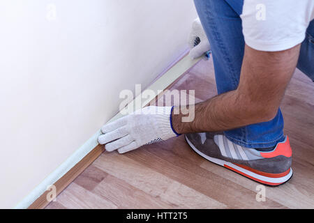 Protezione dei lavoratori dello zoccolo e pavimenti in laminato con del nastro adesivo protettivo prima della verniciatura a casa il lavoro di miglioramento. Muro Bianco Foto Stock