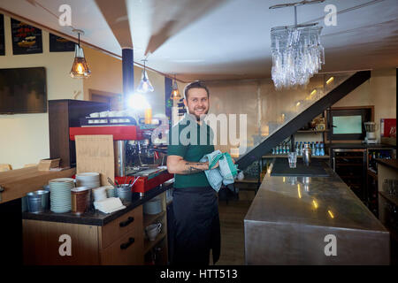 Il barista, barista salviette di lavoro il vetro con un panno in un ristorante dietro al bar. Foto Stock