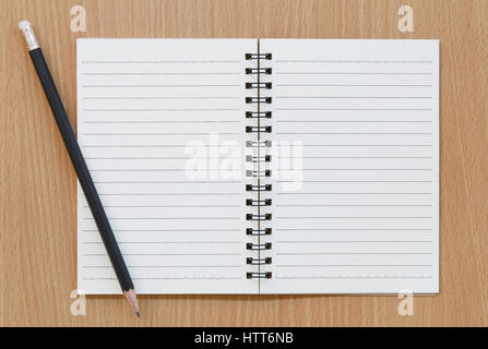 Notebook vuota e matita nera collocata su di un legno marrone dello sfondo. Foto Stock