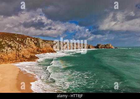 Guardando oltre Porthcurno la spiaggia e la baia. Il 28 febbraio 2017. Dark nuvole temporalesche passando sopra. Con il bel sole d'inverno e una marea. © Barry Foto Stock