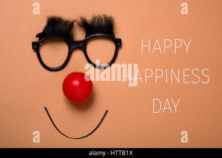 Il testo happy felicità giorno e un paio di occhiali con folte sopracciglia, un rosso clown naso e un sorriso disegnato su uno sfondo marrone Foto Stock