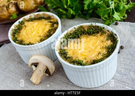 Piatto caldo di funghi, pollo cotto in una salsa cremosa (besciamella), al di sotto di una crosta di formaggio, verde decorazione, in piccole ciotole di ceramica su sfondo scuro Foto Stock