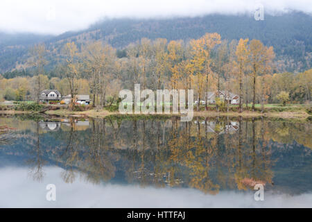 Colori d'autunno gli alberi si riflette nelle calme acque del fiume Fraser Valley, lungo l'autostrada Lougheed, nei pressi di missione, British Columbia, Canada. Foto Stock