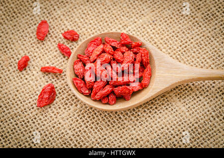 Bacche di goji in cucchiaio di legno su sfondo di sacco. Foto Stock