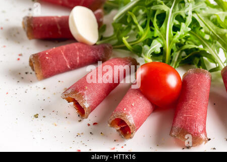 Sottili fette di prosciutto su sfondo bianco. Il Prosciutto, vino, uva, parmigiano sul tavolo di legno, fuoco selettivo. Prosciutto cotto con pomodori o olive e lasciare Foto Stock