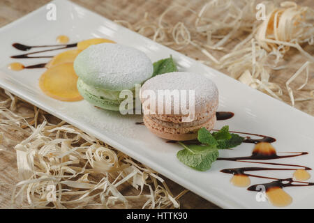 Amaretti colorati in una confezione regalo e marshmallow nella tazza di caffè sul tavolo di legno. Macarons dolci e fiori. Vista superiore Foto Stock