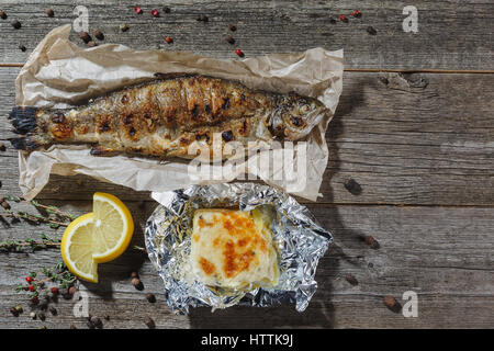 La frittura di pesce sulla piastra bianca con coltello e forchetta, primo piano. Grigliata di pesce di sgombro con patate al forno su un tavolo di legno. Foto Stock