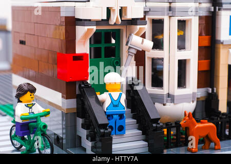 Tambov, Federazione Russa - Gennaio 04, 2017 Lego pittore pittura muro di casa all'esterno. Lego ragazza bicicletta equitazione lungo la strada di casa. Cane Foto Stock