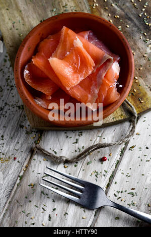 Alta angolazione di un vaso di terracotta con alcune fette di salmone affumicato, su una tavola in legno rustico Foto Stock