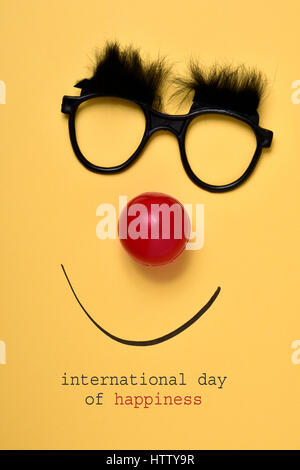 Il testo giornata internazionale della felicità, e un paio di occhiali con folte sopracciglia, un rosso clown naso e un sorriso disegnato su uno sfondo giallo Foto Stock