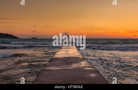 Lone uomo in piedi alla fine del molo con onde che si infrangono su di lui al tramonto. Corfu Grecia Foto Stock