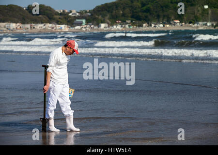 KAMAKURA, Giappone - CIRCA APR, 2013: giapponese uomo trova alimento di mare dopo l'acqua alta sul profondo nella spiaggia di Nagai. La bassa marea acqua è sulla costa dell'oceano pacifico Foto Stock