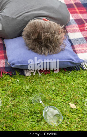 L'Uomo sdraiato in giardino con pelo caduto vino vuote di vetro in erba Foto Stock