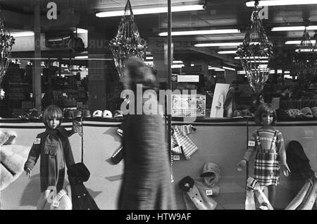 Immagine di archivio di una femmina di shopper camminare davanti a un display di Natale di abbigliamento per bambini in un grande magazzino vetrina, Lambeth, Londra, Inghilterra, 1979, sfocatura del movimento Foto Stock