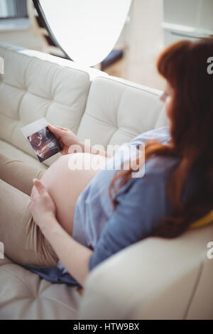 Donna incinta rilassante sul divano e guardando ecografia Foto Stock