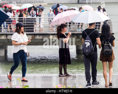 Persone che trasportano gli ombrelli in un giorno di pioggia nella Marina Bay di Singapore. Foto Stock