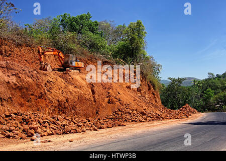 Enorme massa di taglio con pesanti per la costruzione e il movimento terra equipaggiamento idraulico essendo fatto per allargare in autostrada in un terreno collinare Foto Stock