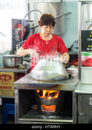 Una donna di Singapore per la cottura e ladling un Nyonya tradizionale zuppa di curry piatto da una pentola. Foto Stock