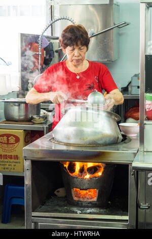 Una donna di Singapore per la cottura e ladling un Nyonya tradizionale zuppa di curry piatto da una pentola. Foto Stock