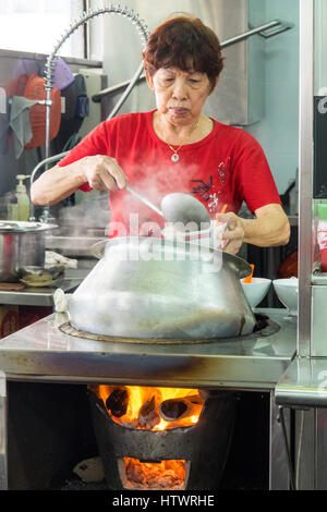 Una donna di Singapore per la cottura e ladling un Nyonya tradizionale zuppa di curry piatto da una pentola. Foto Stock