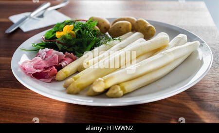 Germania Berlino. Cena a base di asparagi, cibo preferito in primavera. Piastra bianca con asparagi, prosciutto, insalata verde e bolliti potoes Foto Stock