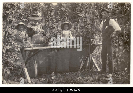 Cartolina originale edoardiana anni '1900 di famiglia che si diverte in una vacanza di lavoro con il hop picking, posando accanto a un hop bin, raccoglitori di hop vittoriani, Regno Unito intorno al 1905 Foto Stock