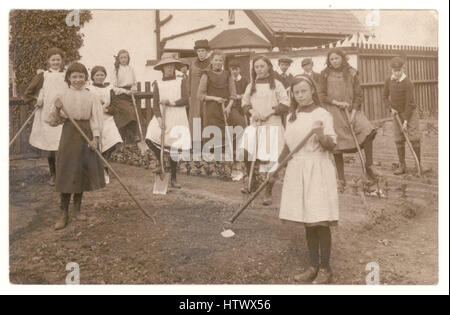 Cartolina originale di bambini, ragazze e ragazzi della scuola britannica, scavando una trama vegetale che aiuta lo sforzo di guerra del WW1, lezione di giardinaggio o progetto. Le classi durante il WW1 sono state spesso tolse la scuola per lavorare sui campi. Ortaggi e frutta sono stati coltivati in giardini privati e allotments. Regno Unito - circa 1915 Foto Stock