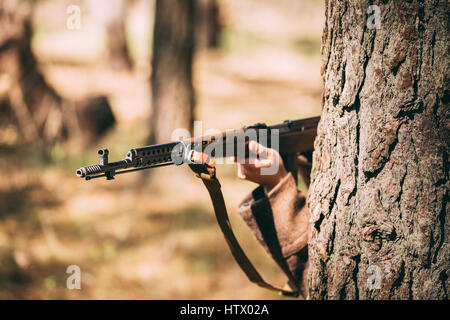 Ri-enactor vestito come Soviet russo Soldato di fanteria della II Guerra Mondiale nascosto con un fucile arma in un agguato nei pressi di albero nella foresta. Chiudere fino a Ri sovietica Foto Stock