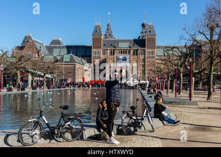 I turisti prendendo un selfie in Amsterdam con un iPhone con la Iamsterdam segno e il Rijksmuseum sullo sfondo Foto Stock