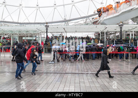 La folla di persone in coda sotto la pioggia battente con ombrelloni in attesa di bordo del London Eye, London, Regno Unito Foto Stock