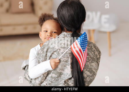 Felici di avervi qui. Grazioso e affascinante ragazza carina abbraccia la sua mamma strettamente mentre saluto la sua casa e tenendo in mano una bandiera Foto Stock