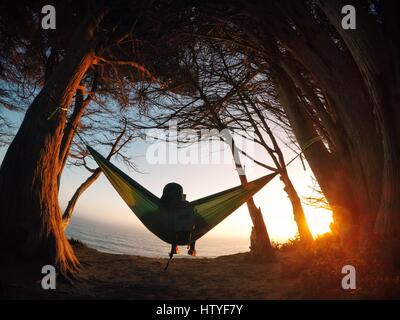 Ragazzo seduto in un'amaca che guarda l'Oceano Pacifico, California, Stati Uniti Foto Stock