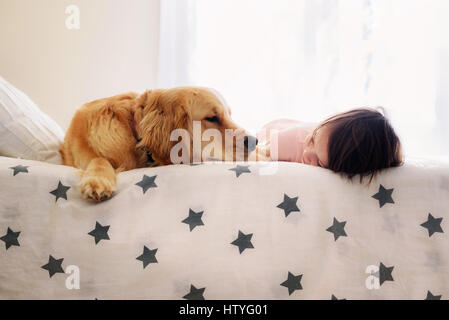 Ragazza sorridente che si trova su un letto accanto a un cane Golden Retriever Foto Stock