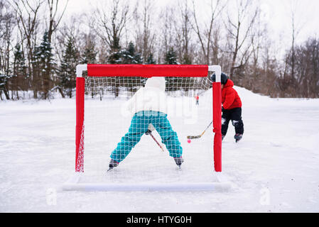 Due bambini che giocano hockey su ghiaccio sul lago ghiacciato Foto Stock