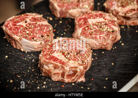 Carne cruda bistecche con spezie sul nero tagliere Foto Stock