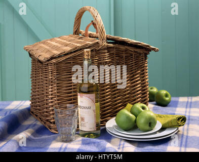 Close-up di una bottiglia di vino bianco sul tavolo con un vintage cestino da picnic e un piatto di mele verdi Foto Stock