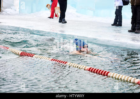 SAHYURTA, Regione di Irkutsk, Russia - marzo 11.2017: Coppa di Baikal. Inverno gare di nuoto. Donna nuota in acqua fredda in berretto lavorato a maglia con pompon Foto Stock