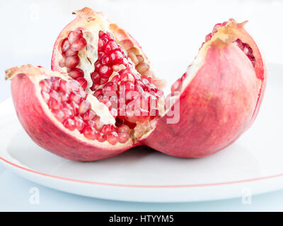 La maturazione dei frutti di melograno e suddiviso in quattro parti, su un bianco piastra di porcellana. La piastra con un confine di melograno. Foto Stock