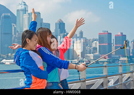 3 teenage Asian Girls prendendo un bastone selfie ritratto con le mani in aria a sorridere e ridere dal Kowloon Public Pier in Hong Kong. Foto Stock