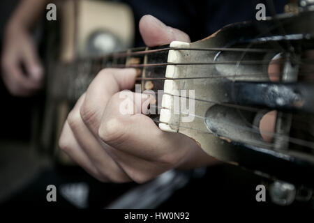 La mano dell'uomo close up contiene una corda su una chitarra Firma Timbro Foto Stock