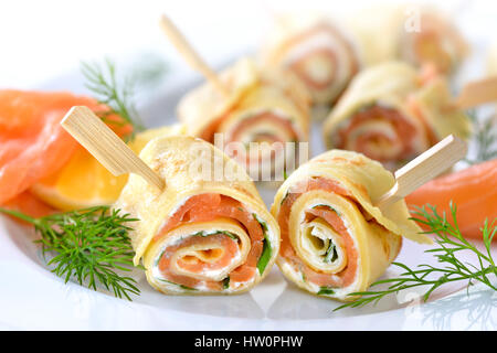 Rotoli di sottili frittelle con salmone affumicato, il rafano crema di formaggio e rucola Foto Stock