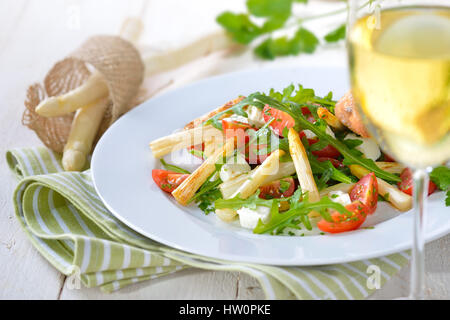 Insalata mista con fried asparagi bianchi, greco il formaggio feta, rucola e pomodori ciliegini, servito con un bicchiere di vino bianco secco Foto Stock