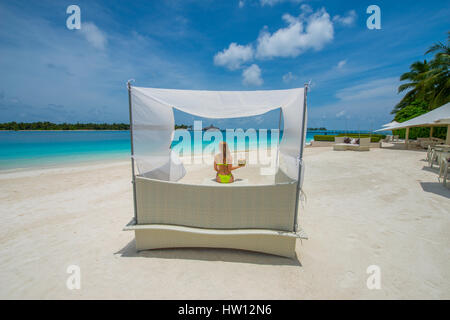 Maldive Rangali Island. Conrad Hilton Resort. Donna seduta nella tettoia sedia sulla spiaggia. (MR) Foto Stock