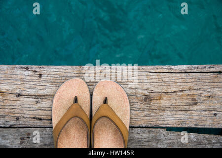 Il beige flip-flop sandali sul bordo della banchina in legno su acqua Foto Stock