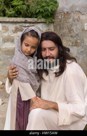 Scena biblica quando Gesù dice, lasciate che i bambini vengano a me, la benedizione di una bambina. La rievocazione storica di un antico pozzo di acqua. Foto Stock